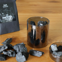 Charcoal pieces in a glass container on a wooden surface with a branded black bag.