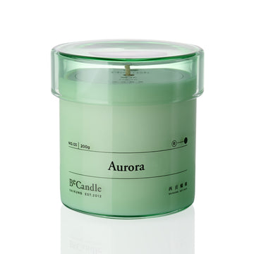 Green candle in a transparent container labeled 'Aurora' on a white background