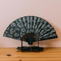 Black hand fan with white patterns on a wooden surface and pink background