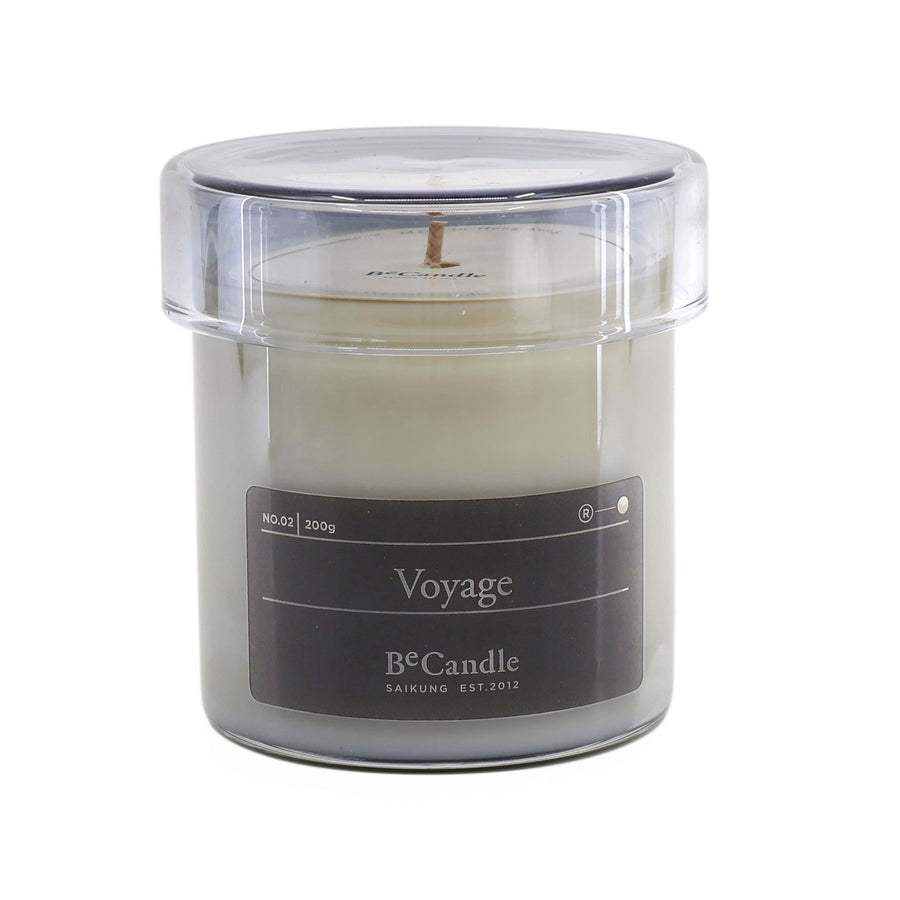 Candle in a clear container labeled 'Voyage' on a white background